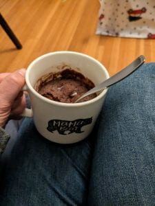 A hand holds a white coffee mug with chocolate cake visible inside of it.